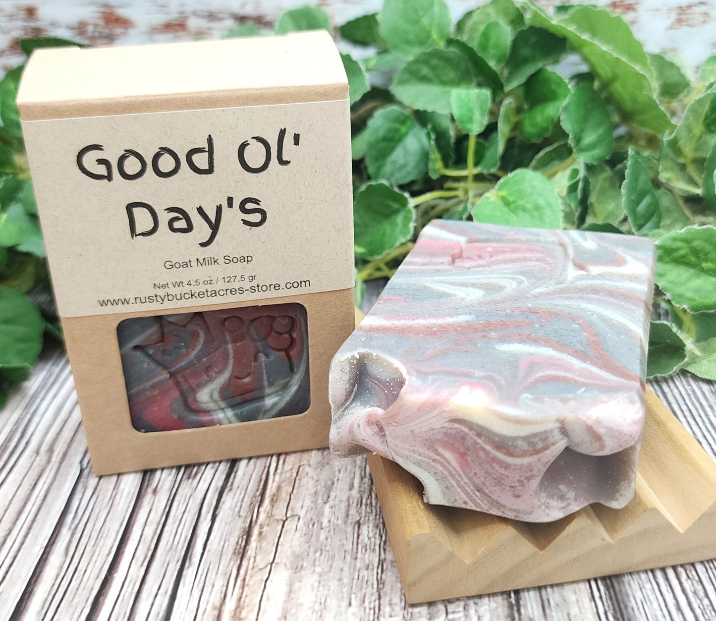 Goat milk soap with a decorative box on a wooden surface with greenery in the background