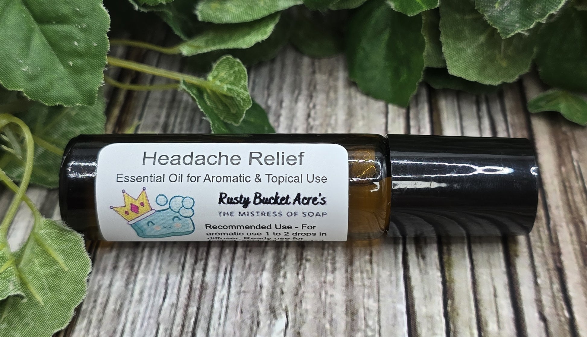 Roll-on bottle of essential oil labeled 'Headache Relief' by Rusty Bucket Ace's on a wooden surface with green leaves.