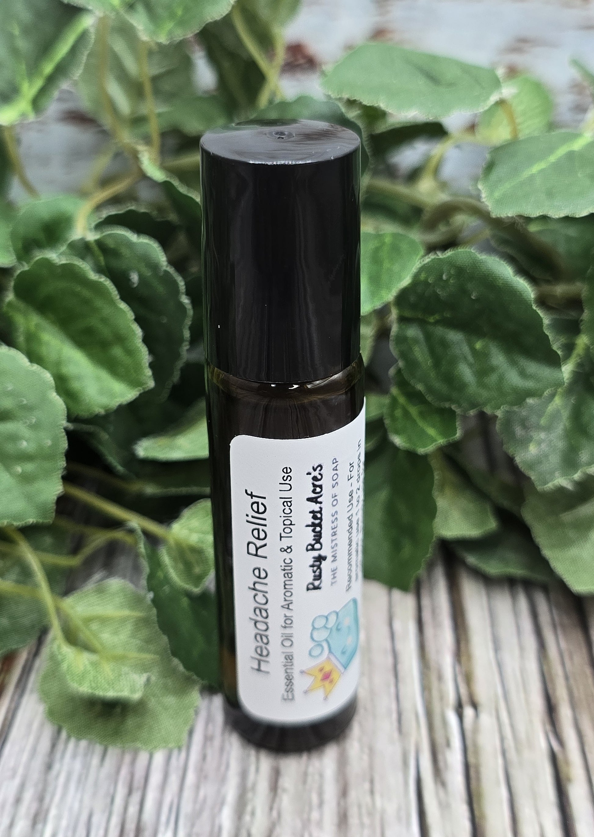 Roll-up bottle of 'Headache Relief' oil by Ruby Ann's on a wooden surface with green leaves in the background