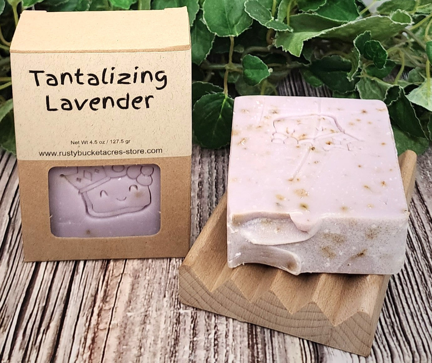 Bar of soap with packaging labeled 'Tantalizing Lavender' on a wooden surface with greenery in the background.