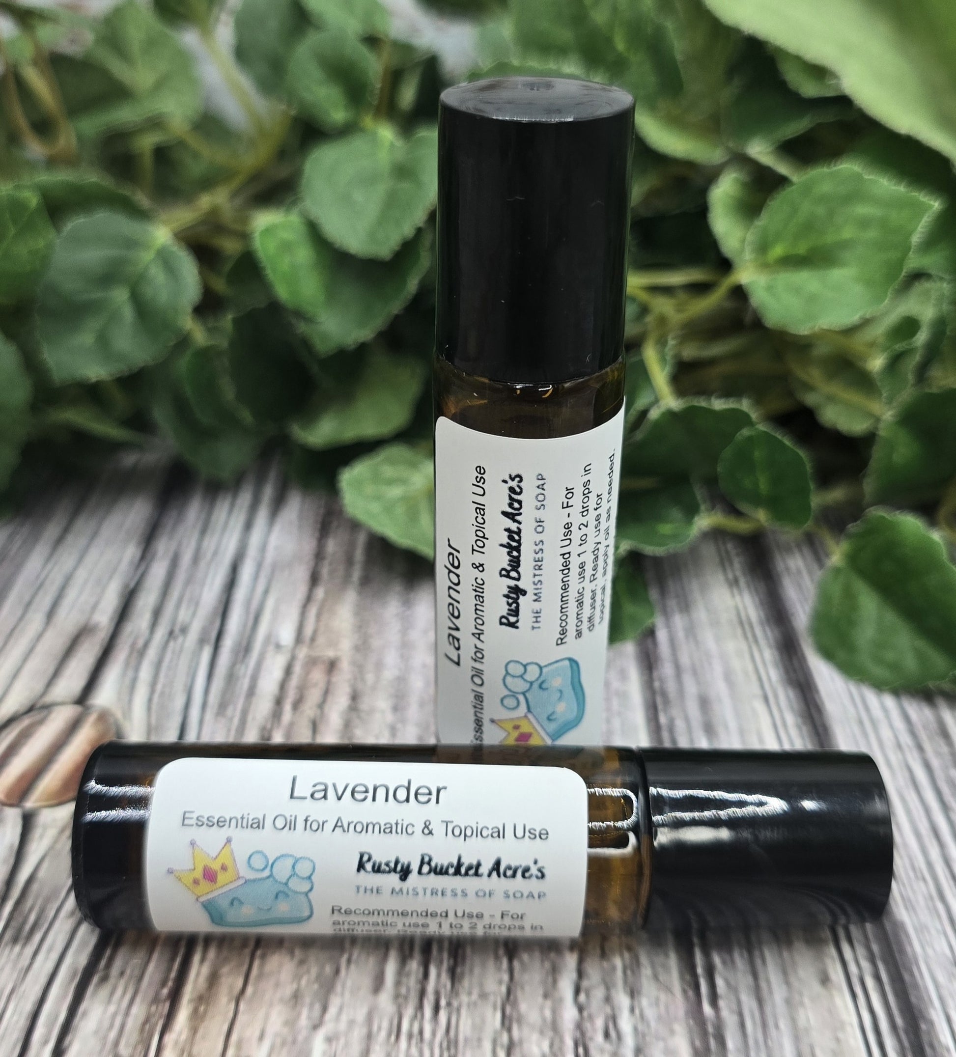 Two bottles of Lavender essential oil with labels on a wooden surface with green leaves in the background.