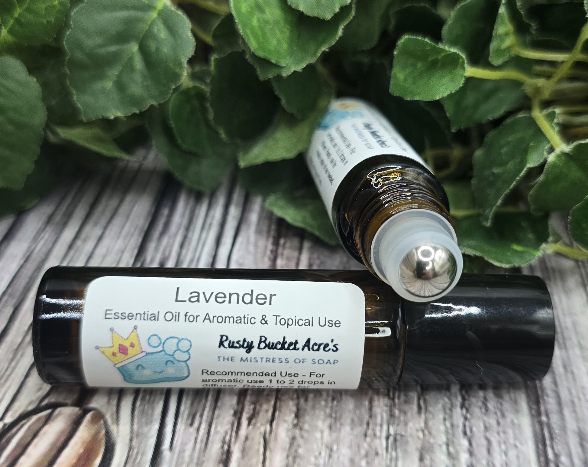 Two bottles of Lavender essential oil on a wooden surface with green leaves in the background