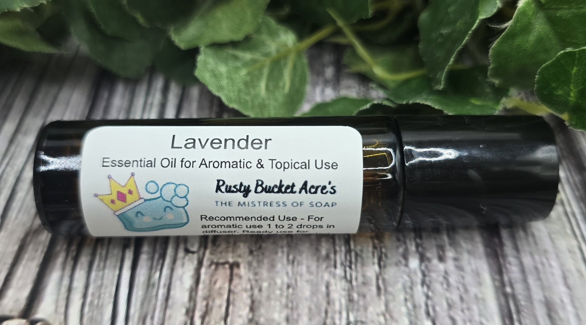 Roll-on bottle of lavender essential oil with a label on a wooden surface with green leaves in the background.