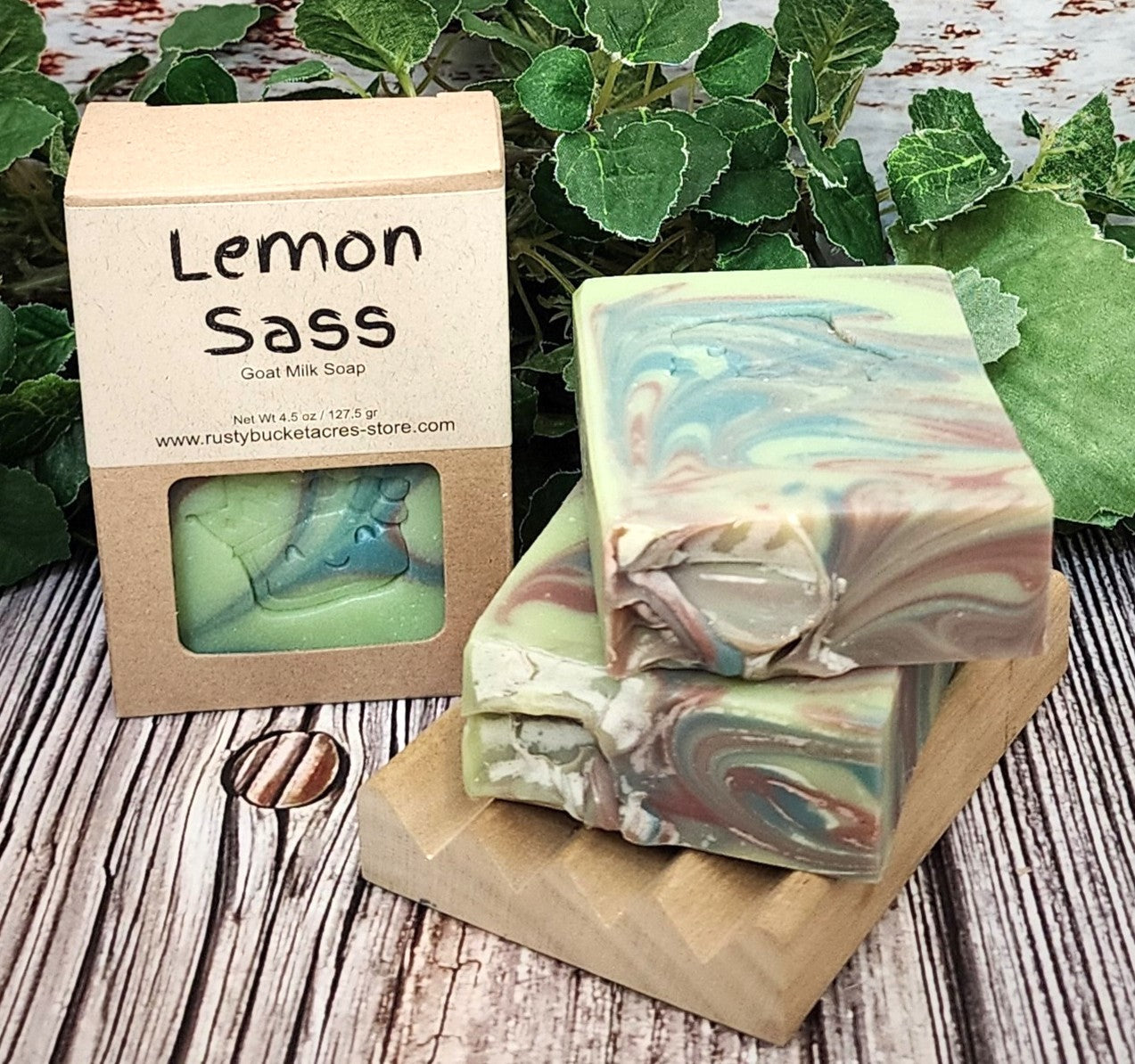 Colorful soap bars with a 'Lemon Sass' packaging on a wooden surface with greenery.