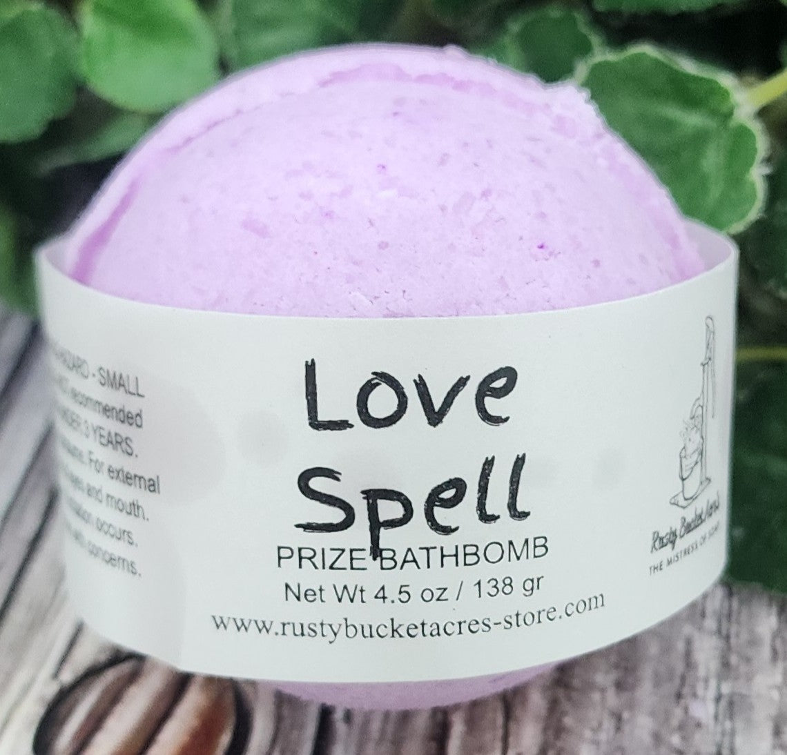 Purple bath bomb with 'Love Spell' label on a green leafy background