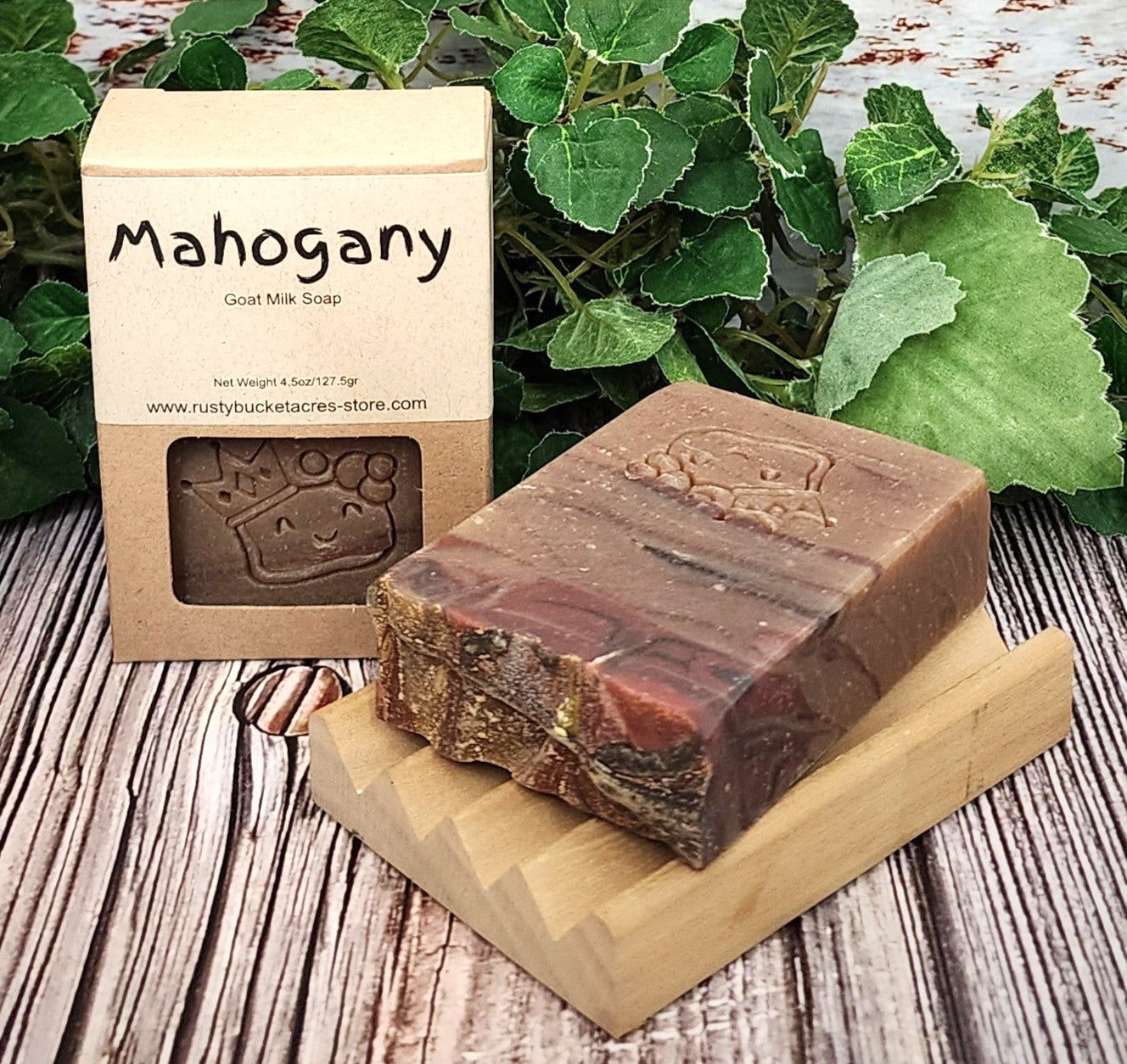 Bar of Mahogany goat milk soap on a wooden stand with packaging and green leaves in the background