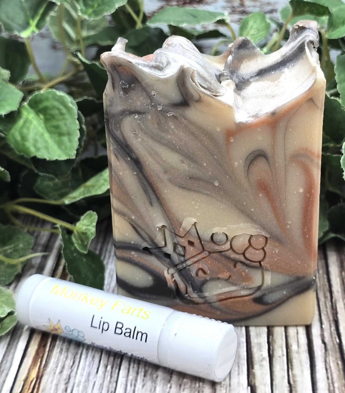 Marbled soap bar and lip balm on a wooden surface with green leaves in the background