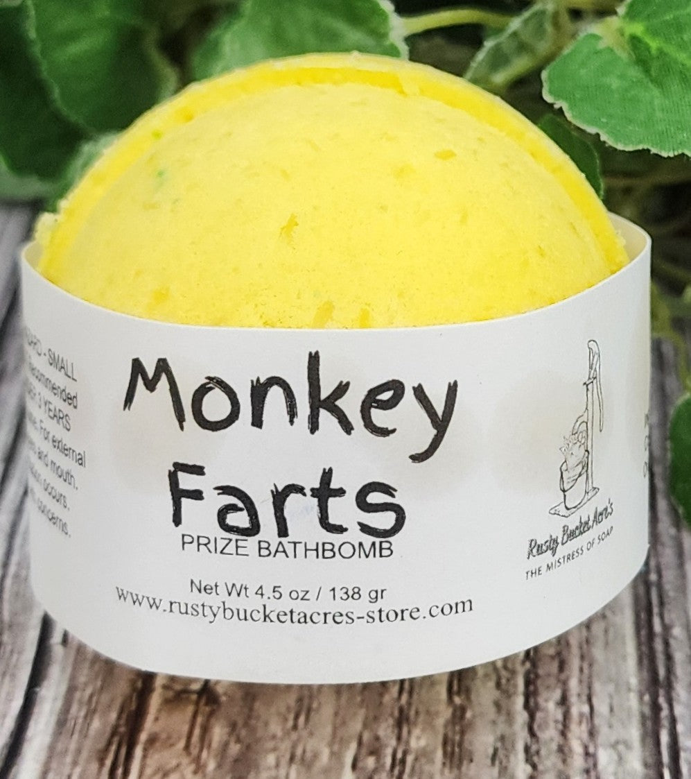 Yellow bath bomb with 'Monkey Farts' label on a wooden surface with green leaves in the background