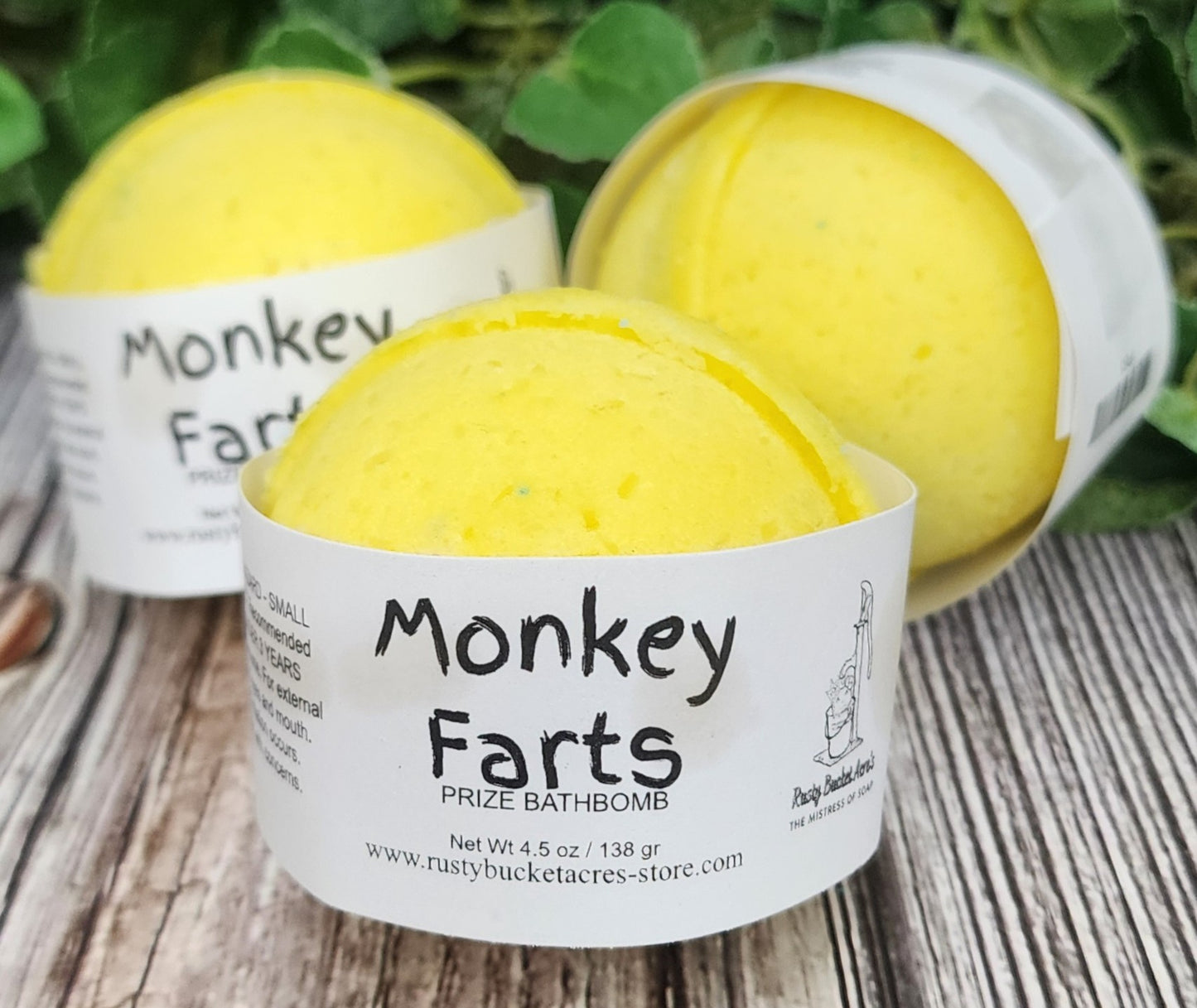 Yellow bath bombs labeled 'Monkey Farts' on a wooden surface with greenery in the background.