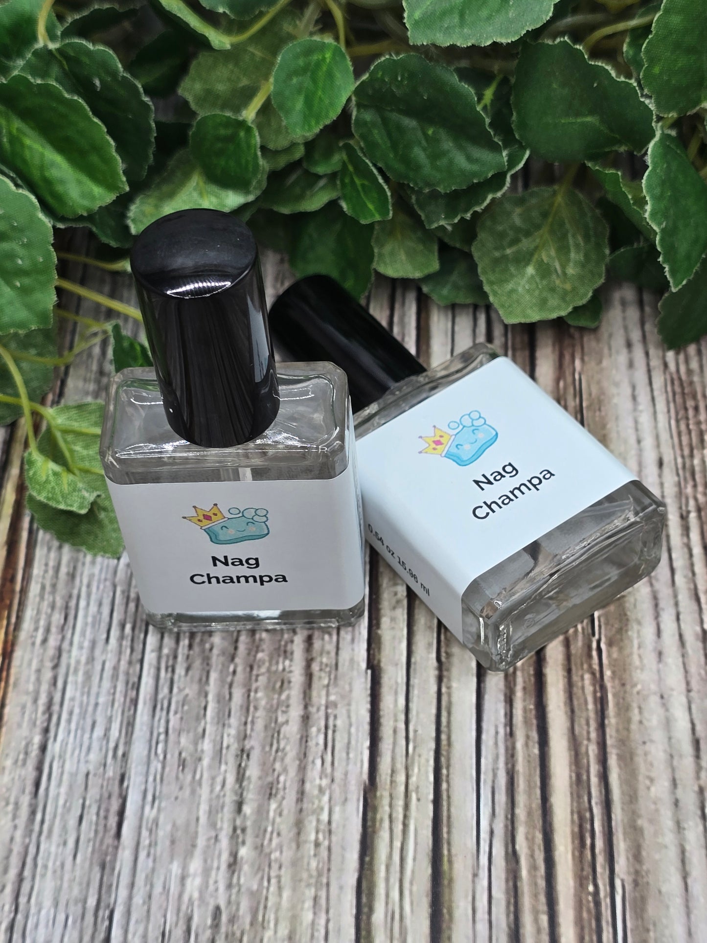 Two Nag Champa perfume bottles on a wooden surface next to green leaves.