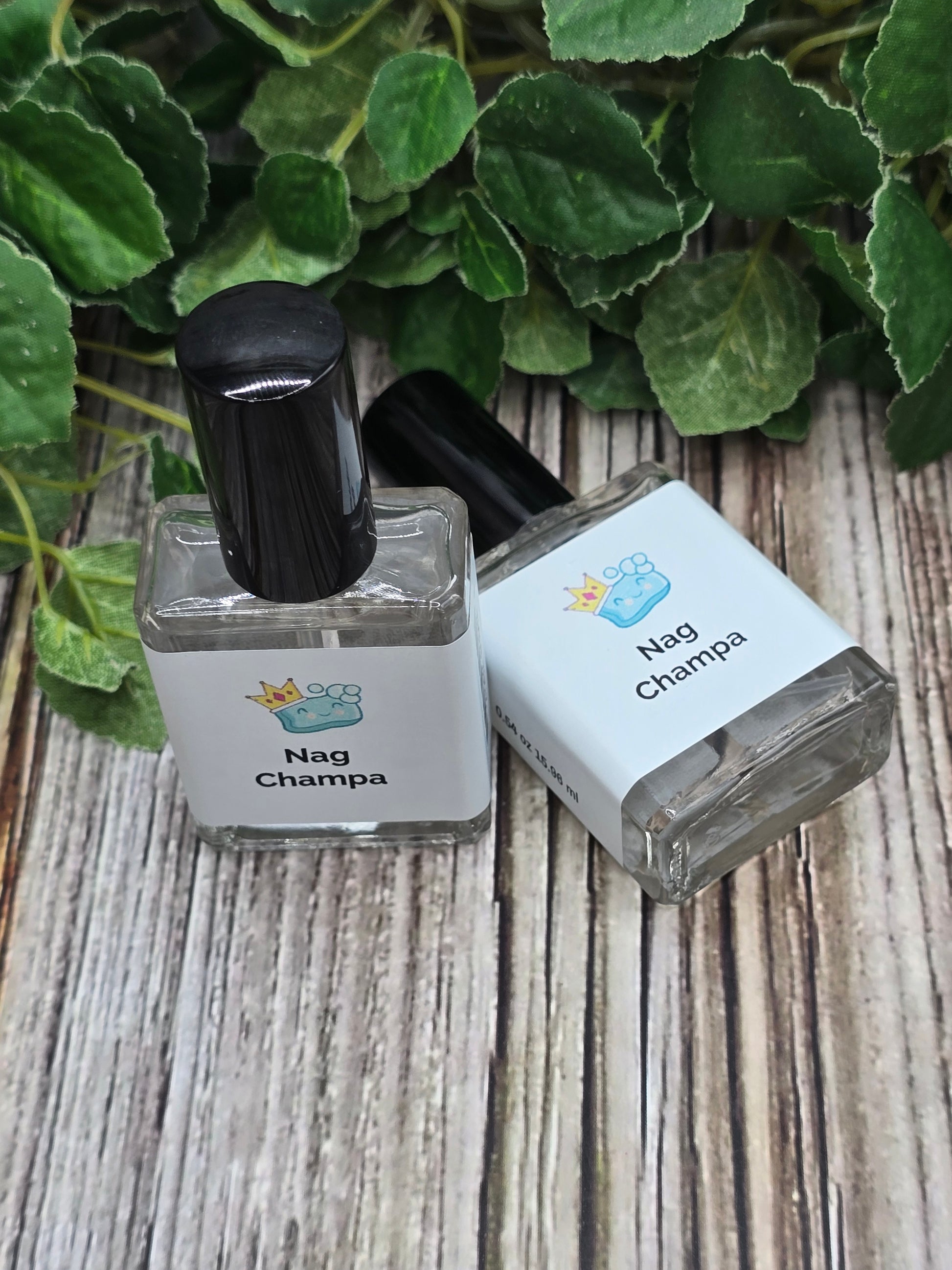 Two Nag Champa perfume bottles on a wooden surface next to green leaves.