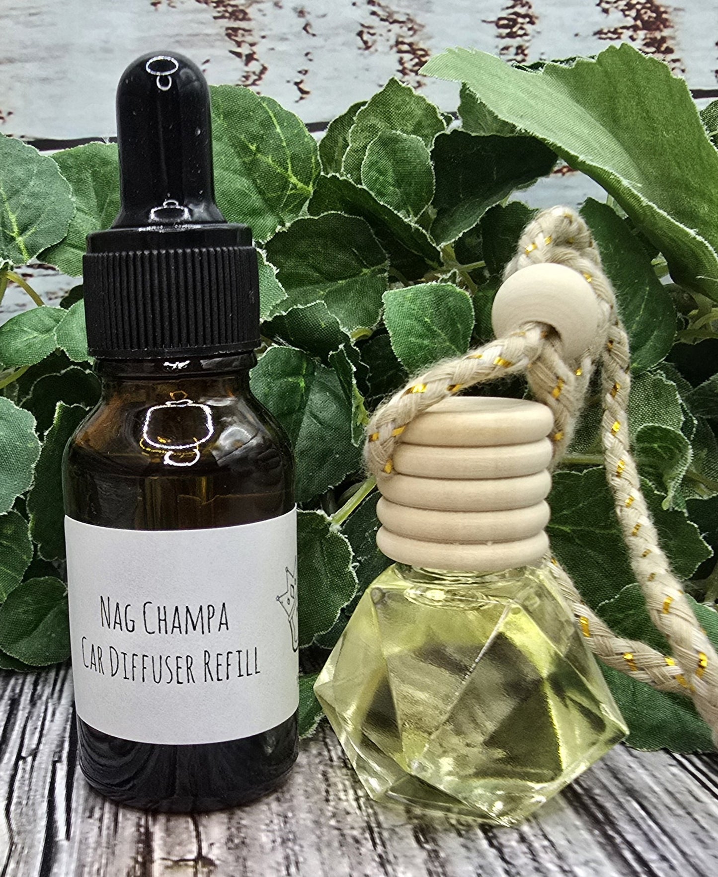 Nag Champa car diffuser refill bottle with a dropper and a clear glass diffuser on a wooden surface with green leaves.
