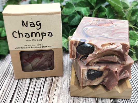 Nag Champa goat milk soap with packaging on a wooden surface and green leaves in the background