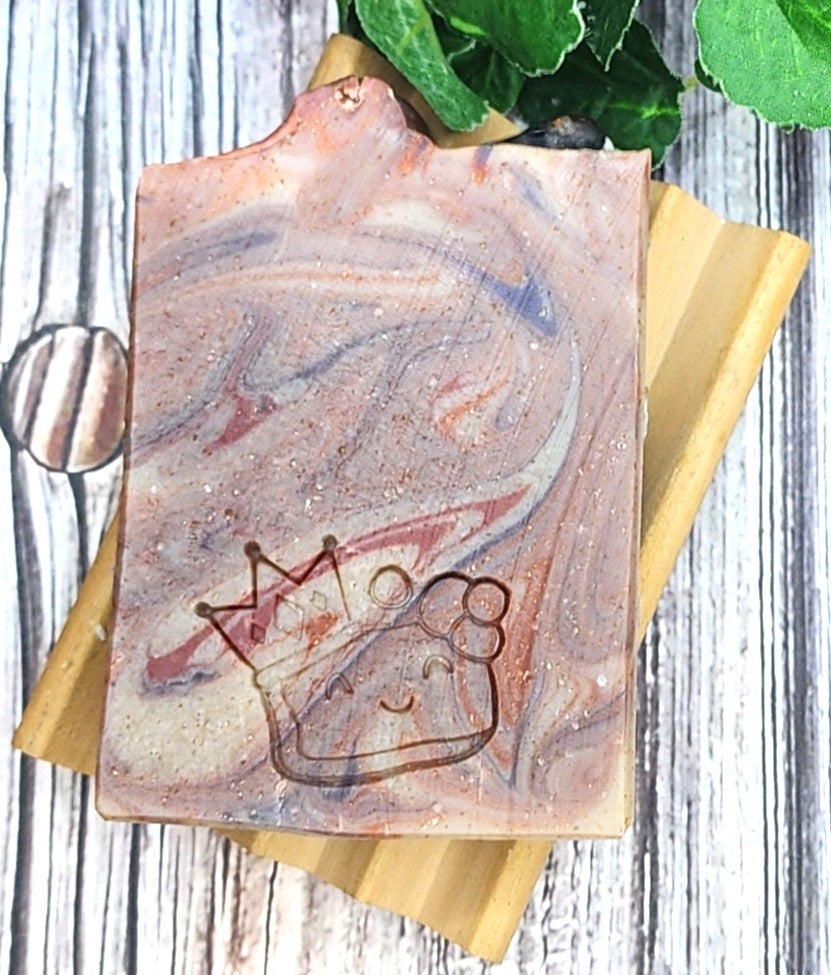 Marble-patterned soap bar with a frog design and crown on a wooden block, against a rustic wooden background.