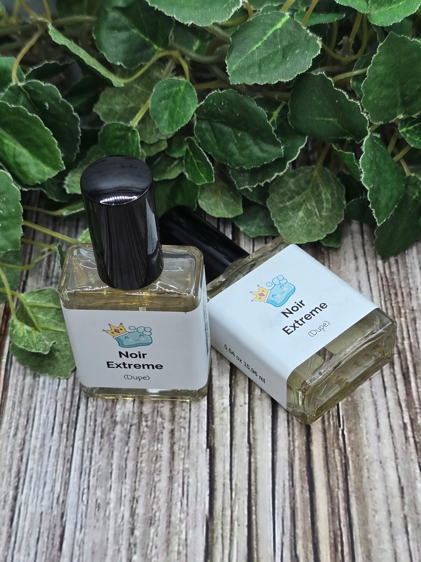 Two bottles of Noir Extreme perfume on a wooden surface with green leaves.