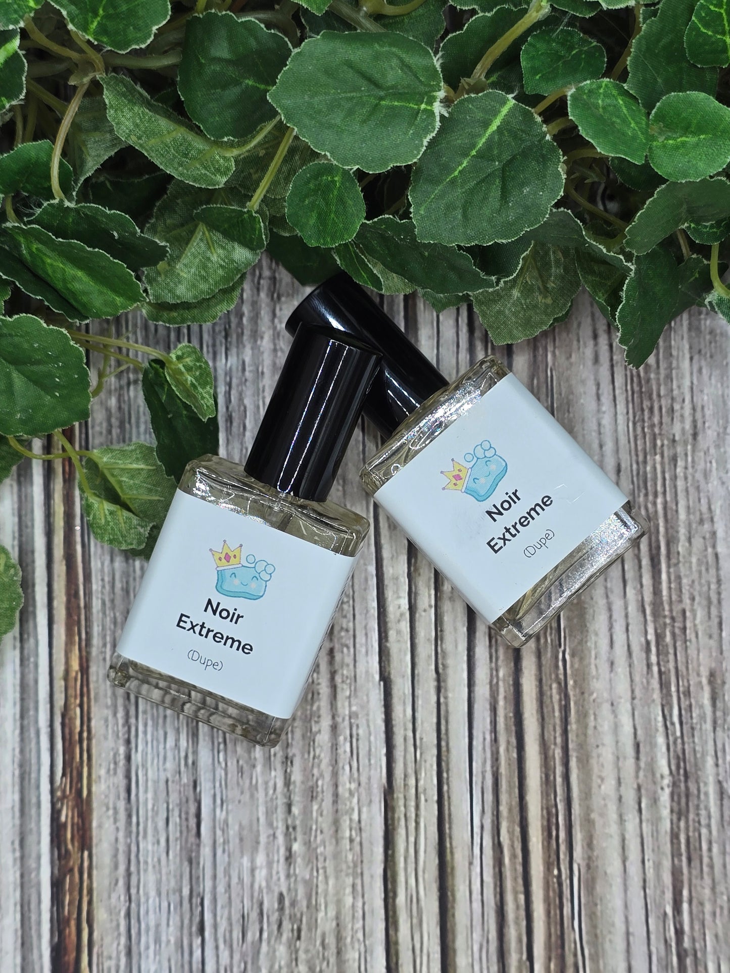 Two bottles of 'Noir Extreme' perfume on a wooden surface with green leaves.