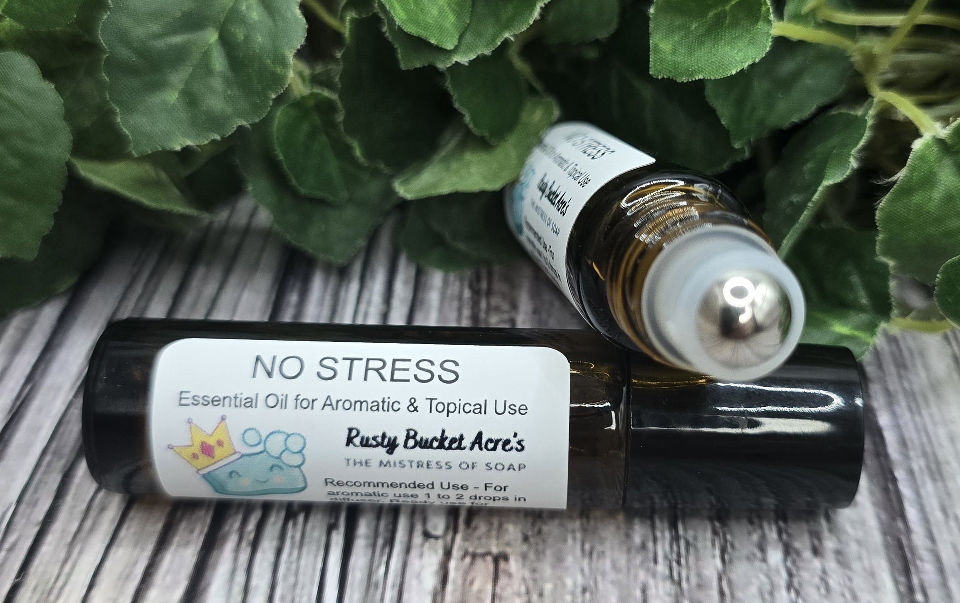 Two essential oil bottles labeled 'NO STRESS' on a wooden surface with green leaves in the background.