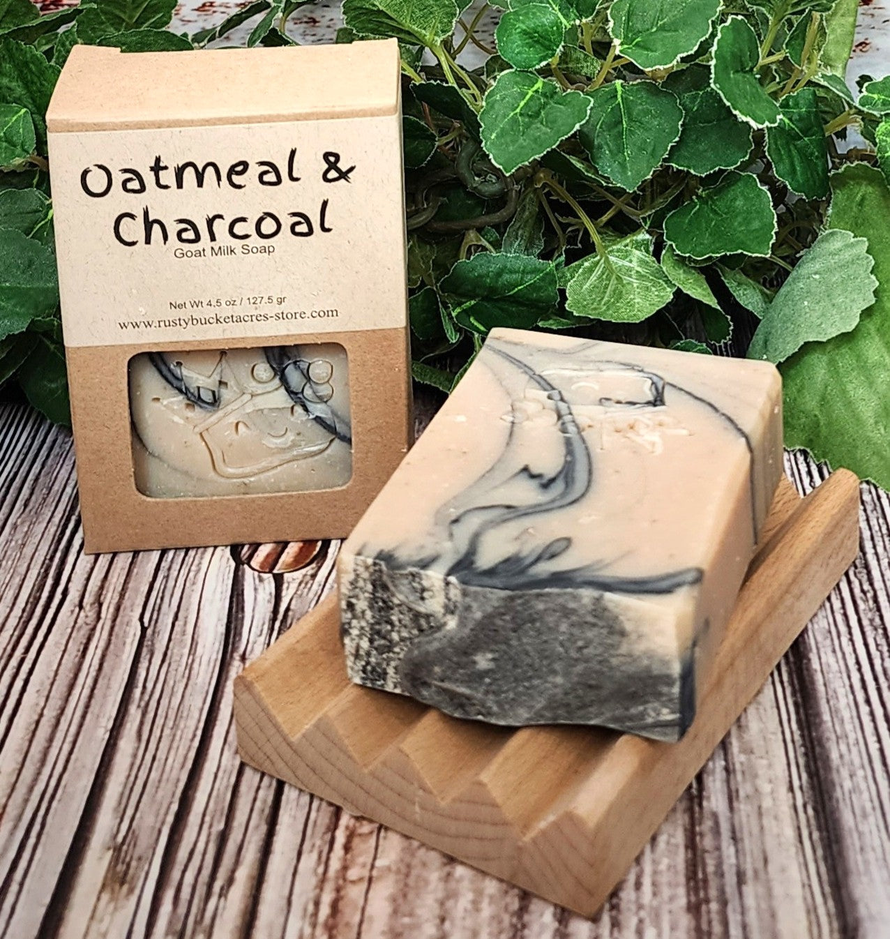 Oatmeal & Charcoal soap bar with packaging on a wooden surface with greenery in the background