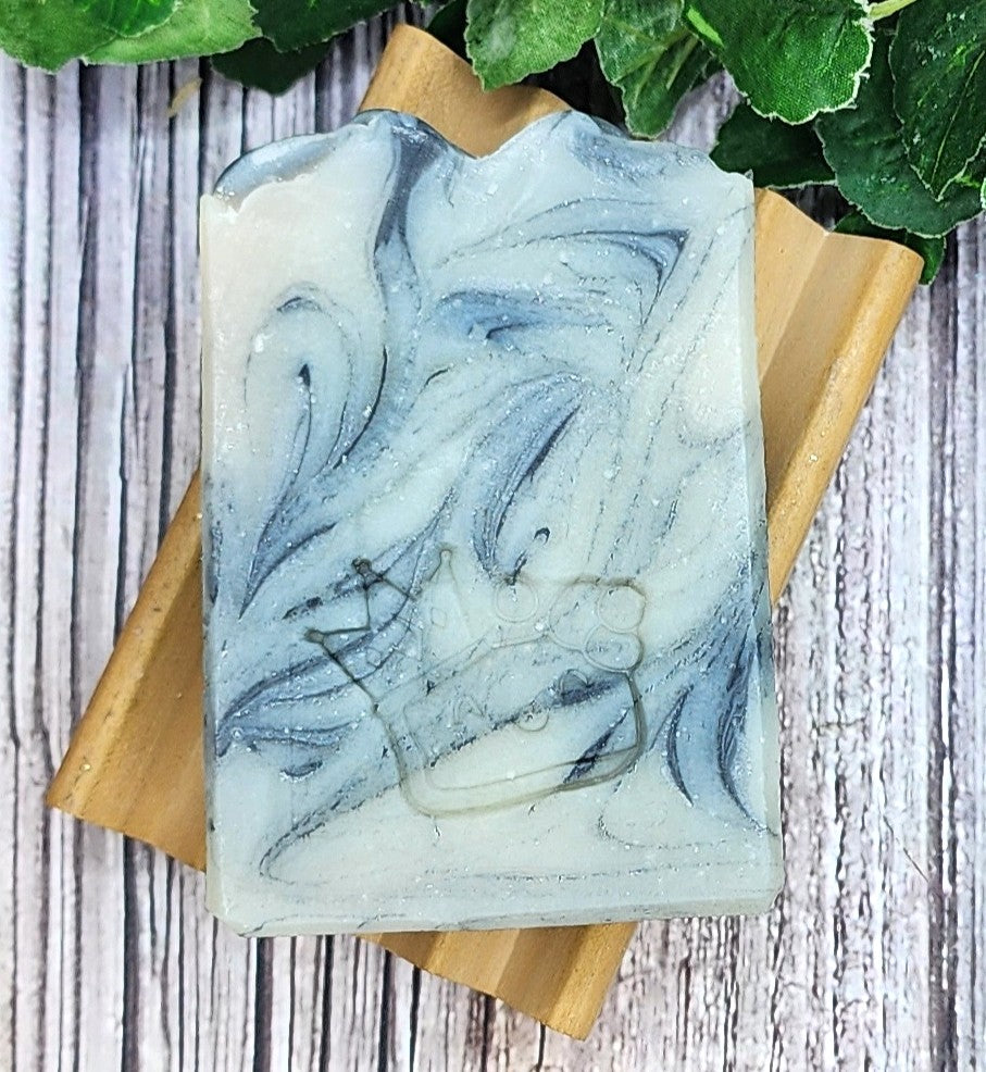 Marbled grey and white soap bar on a wooden soap dish with green leaves in the background
