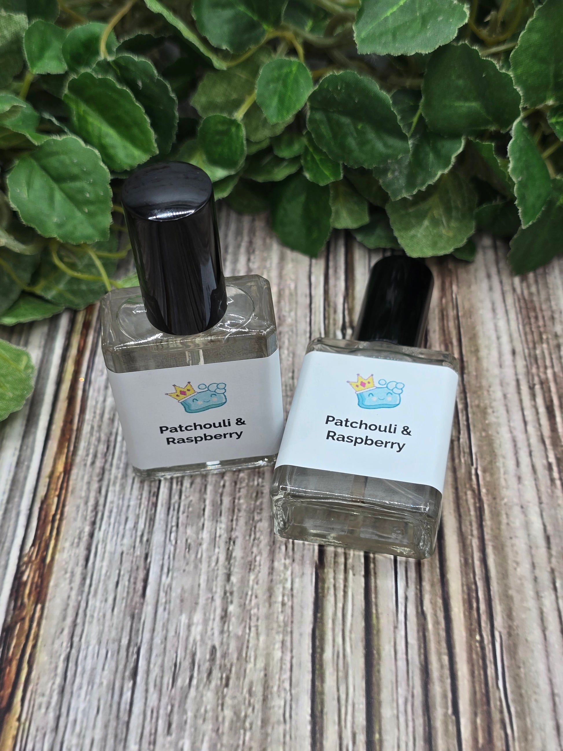 Two small bottles of Patchouli Raspberry perfume on a wooden surface with green leaves.