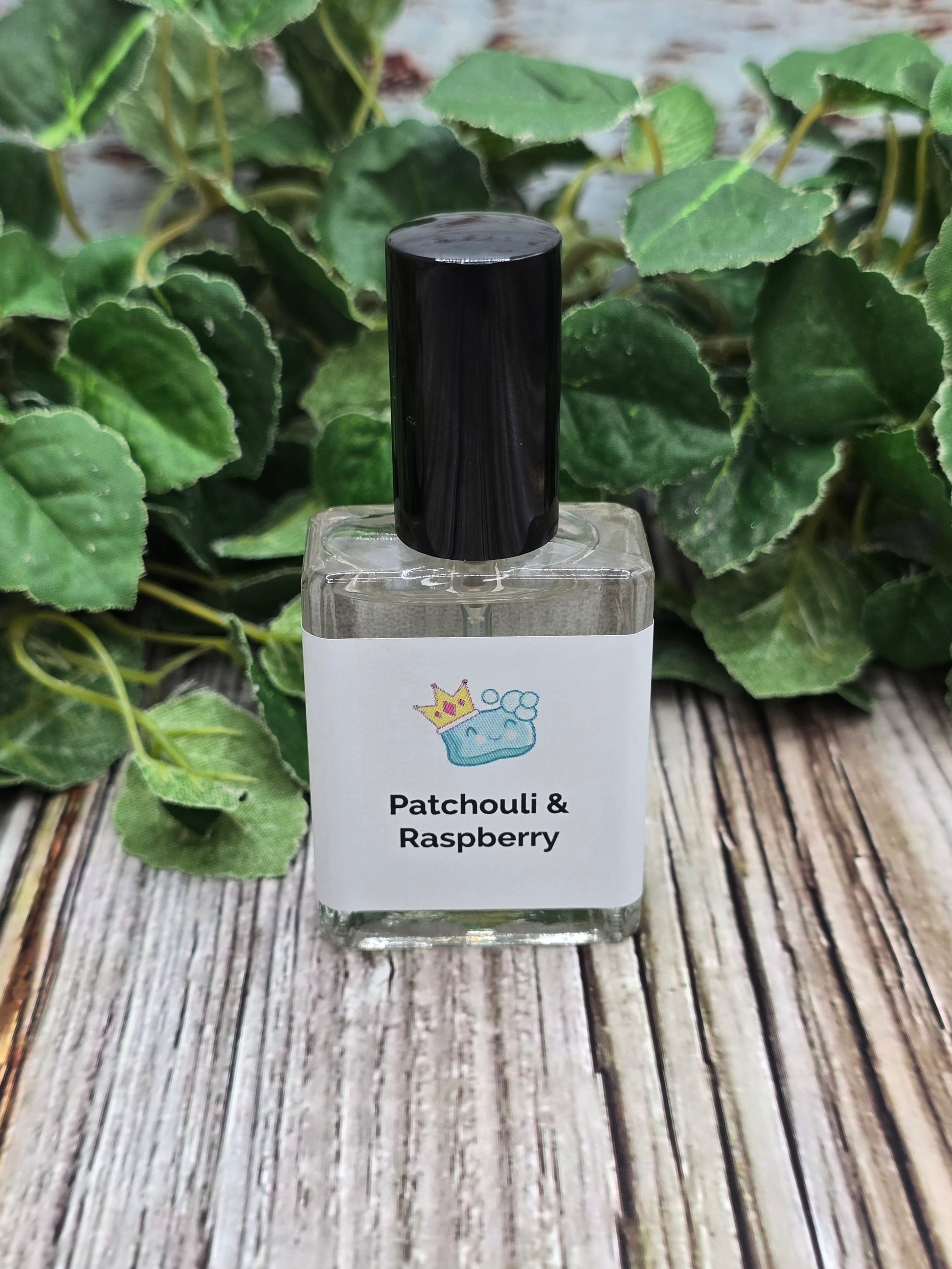 Small bottle of Patchouli & Raspberry perfume on a wooden surface with green leaves in the background.