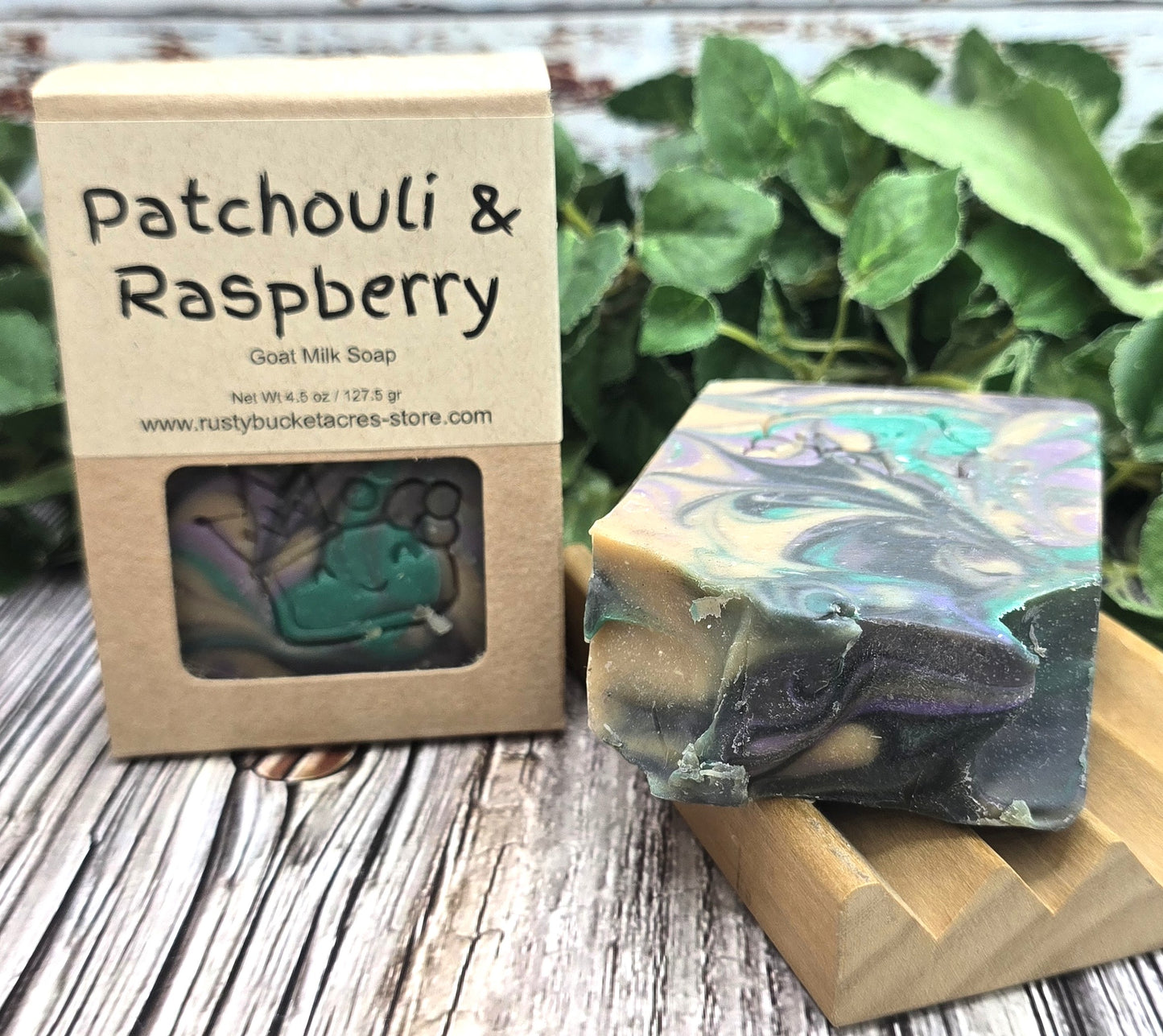 Goat milk soap with patchouli and raspberry scent next to its packaging on a wooden surface.