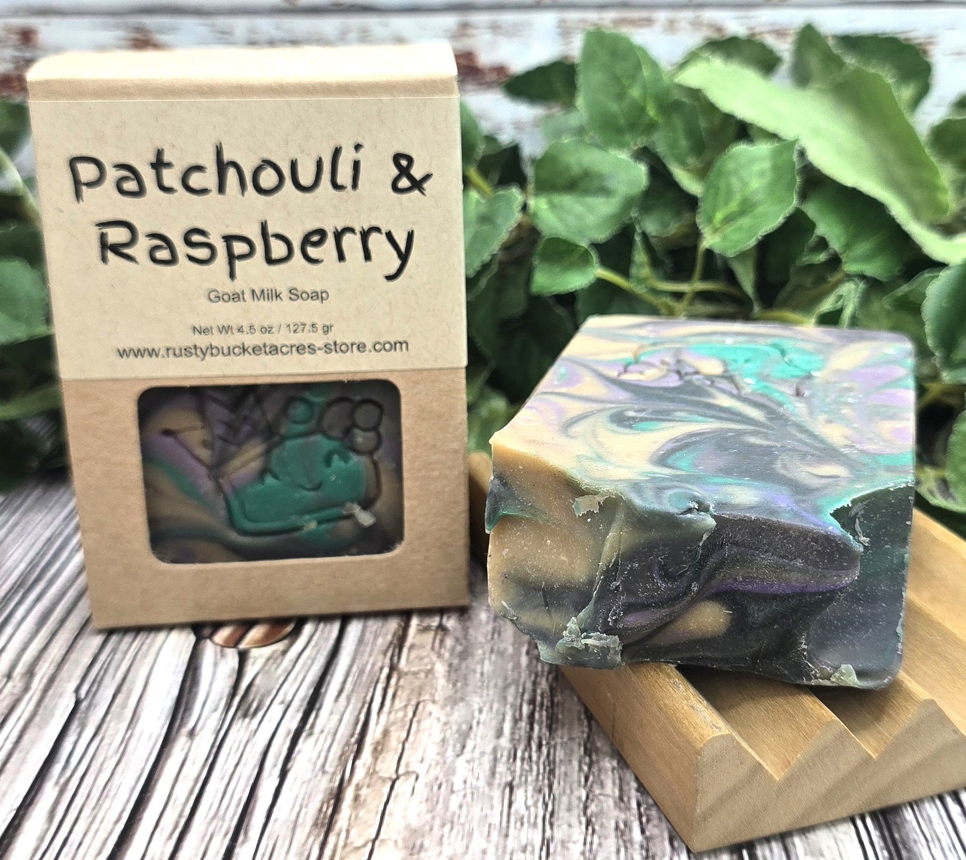 Goat milk soap with patchouli and raspberry scent next to its packaging on a wooden surface.