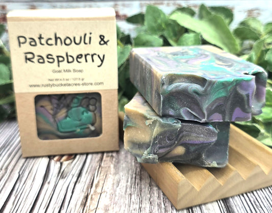 Two bars of Patchouli & Raspberry soap with a box on a wooden surface.