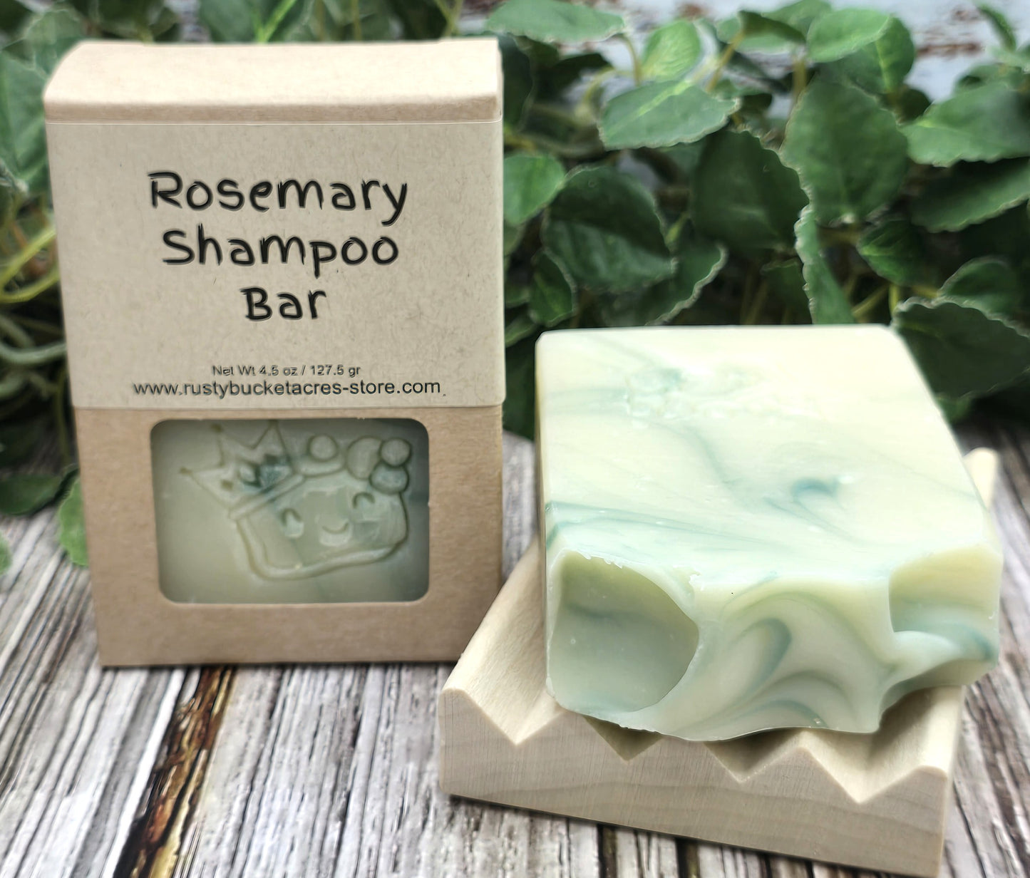 Rosemary shampoo bar with packaging on a wooden surface with greenery in the background