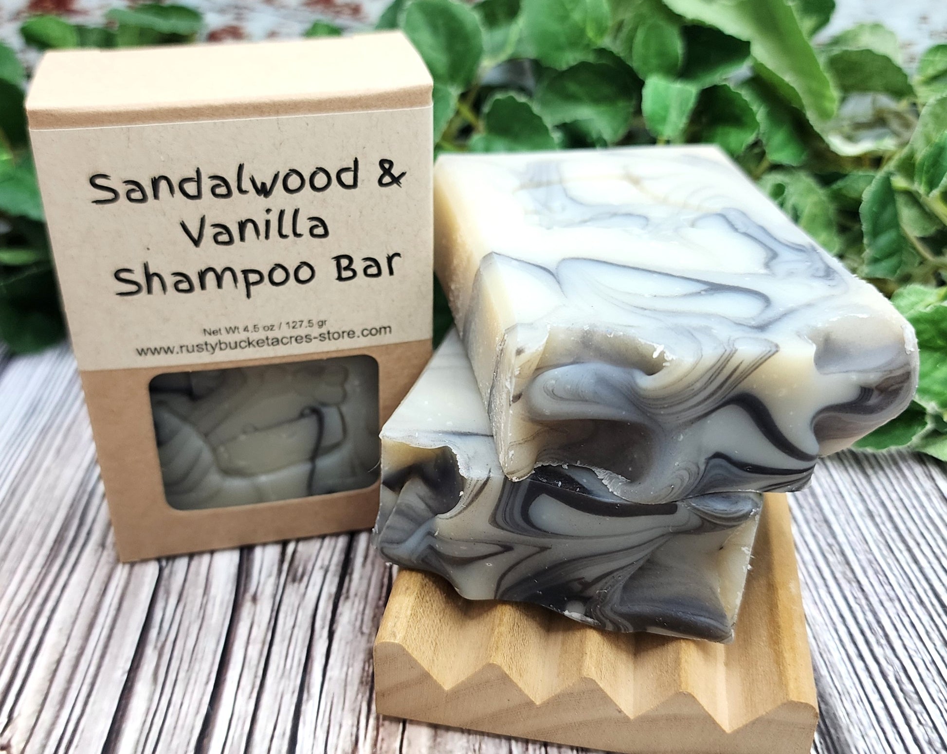 Sandalwood & Vanilla Shampoo Bar with packaging on a wooden surface with greenery in the background