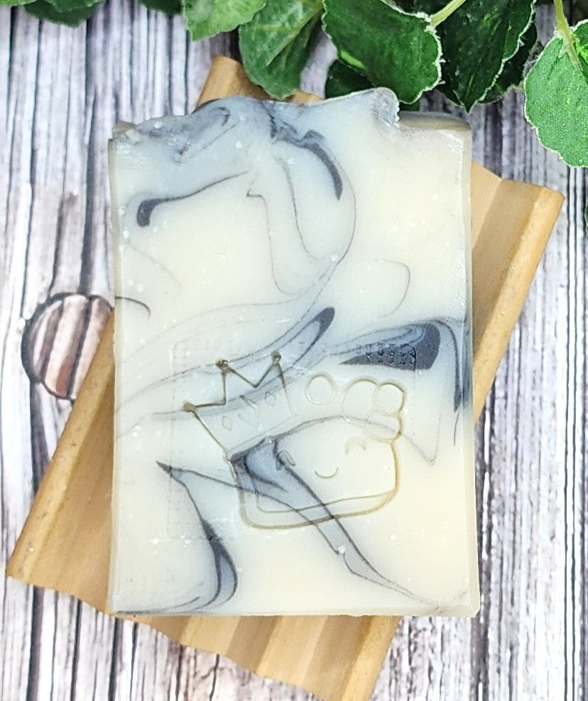 Handmade soap with marble design on a wooden soap dish, surrounded by green leaves.