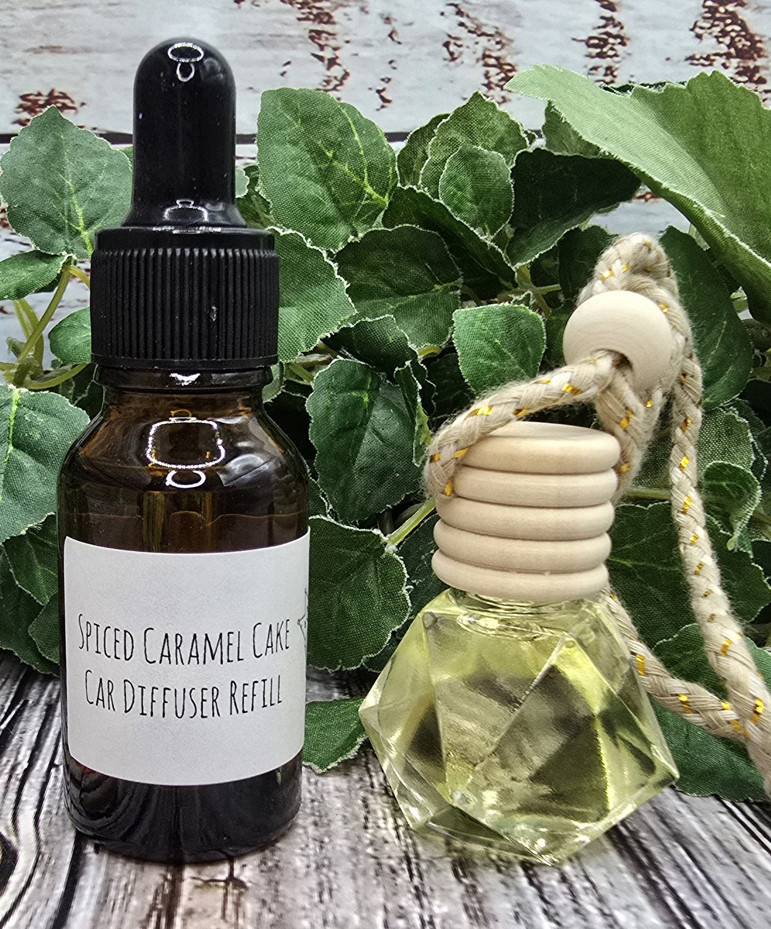 Spiced Caramel Cake car diffuser & refill bottle and wooden diffuser on a wooden surface with green leaves.