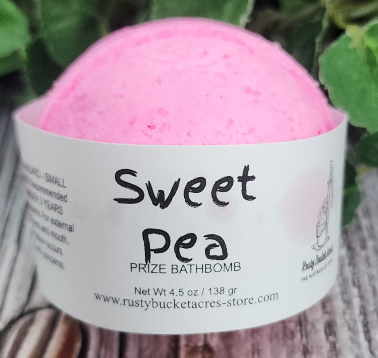 Pink bath bomb with a label on a wooden surface with green leaves in the background