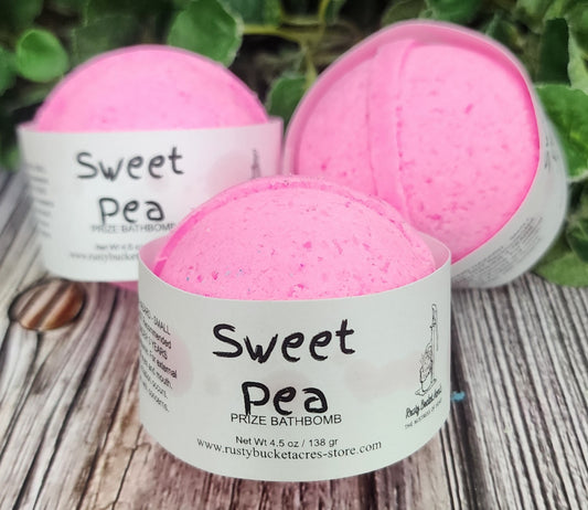 Pink bath bombs labeled 'Sweet Pea' on a wooden surface with greenery in the background.