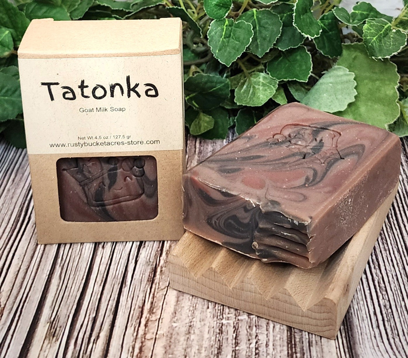 Tatonka goat milk soap with packaging on a wooden surface with green leaves in the background