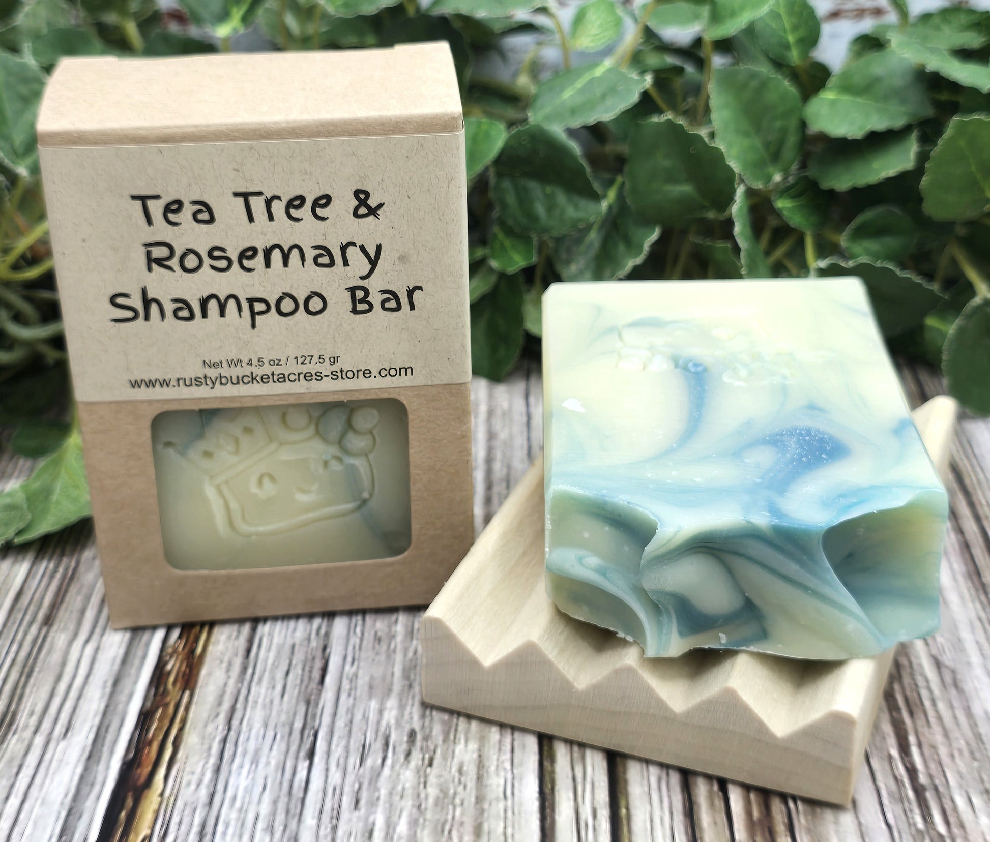Tea Tree & Rosemary Shampoo Bar with packaging on a wooden surface with green leaves in the background