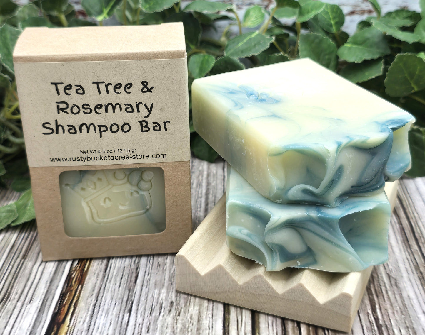 Tea Tree & Rosemary Shampoo Bar with packaging on a wooden surface with greenery in the background