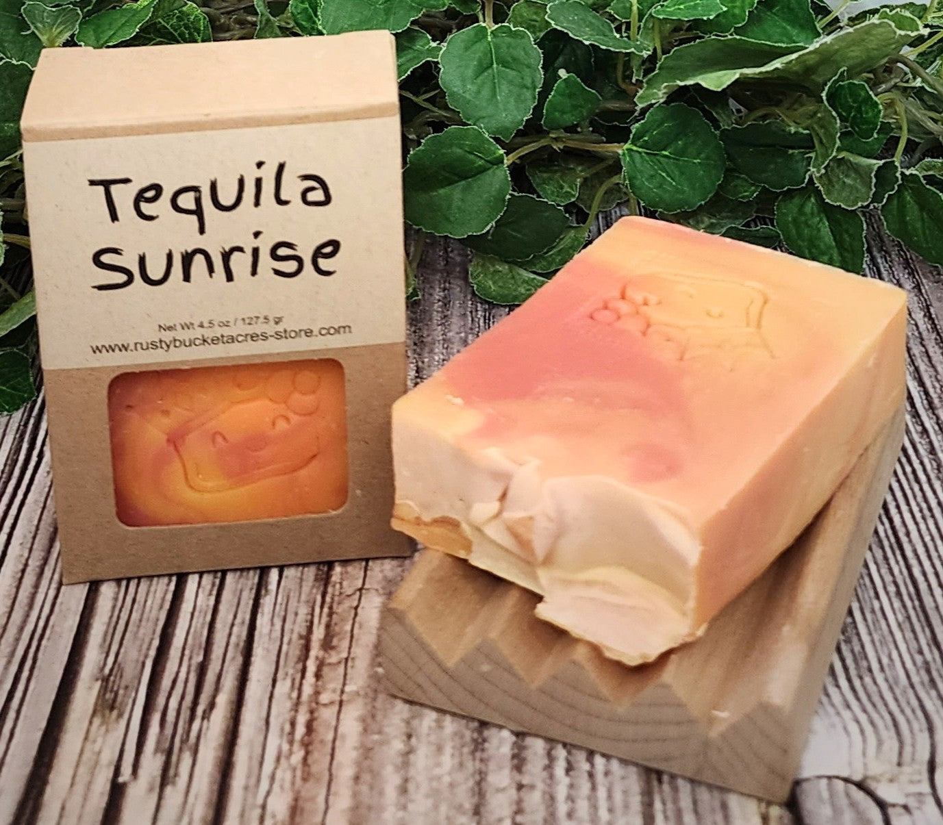 Bar of soap with 'Tequila Sunrise' packaging on a wooden surface with green leaves in the background