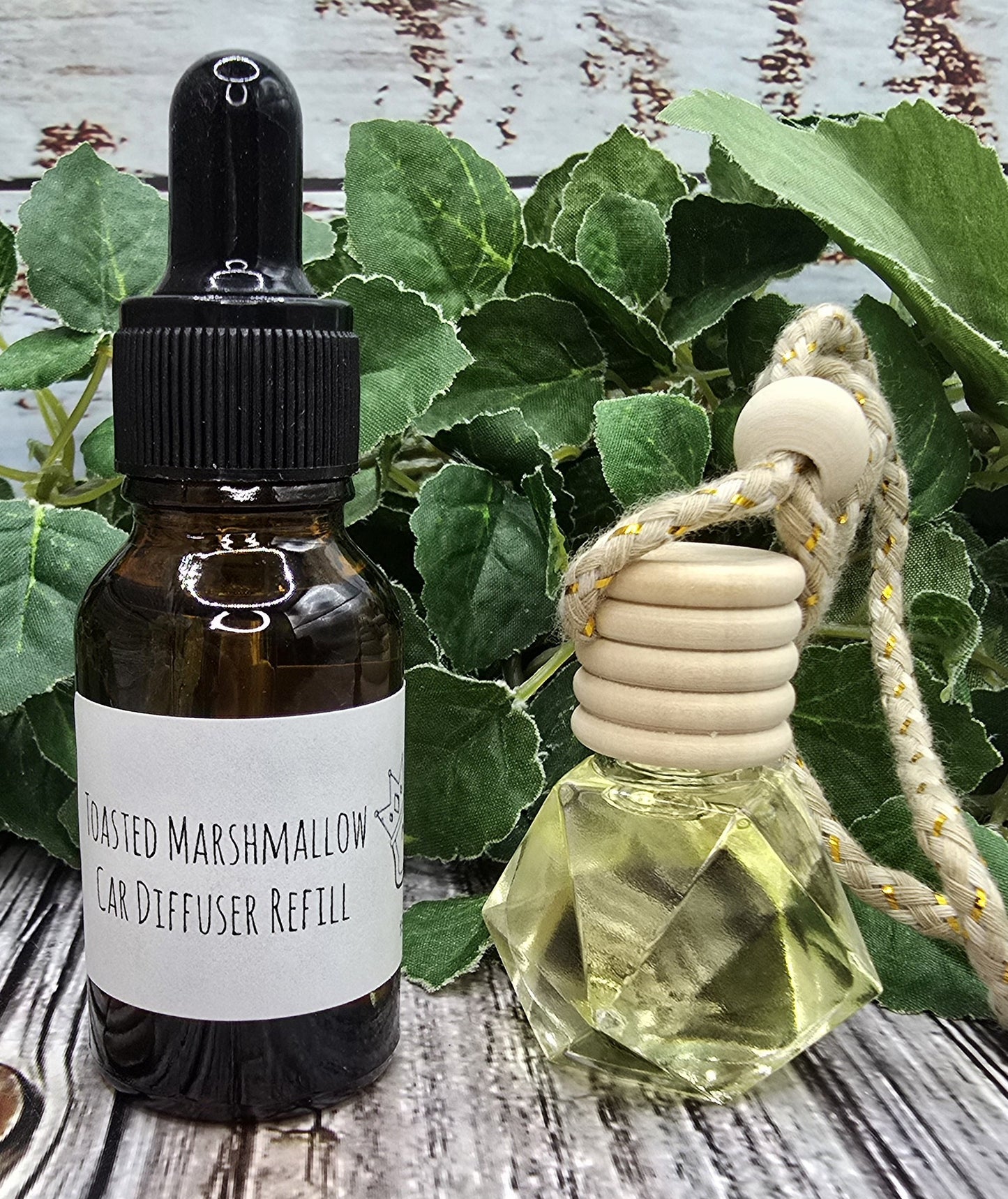 Toasted Marshmallow diffuser & refill on a wooden surface with green leaves in the background