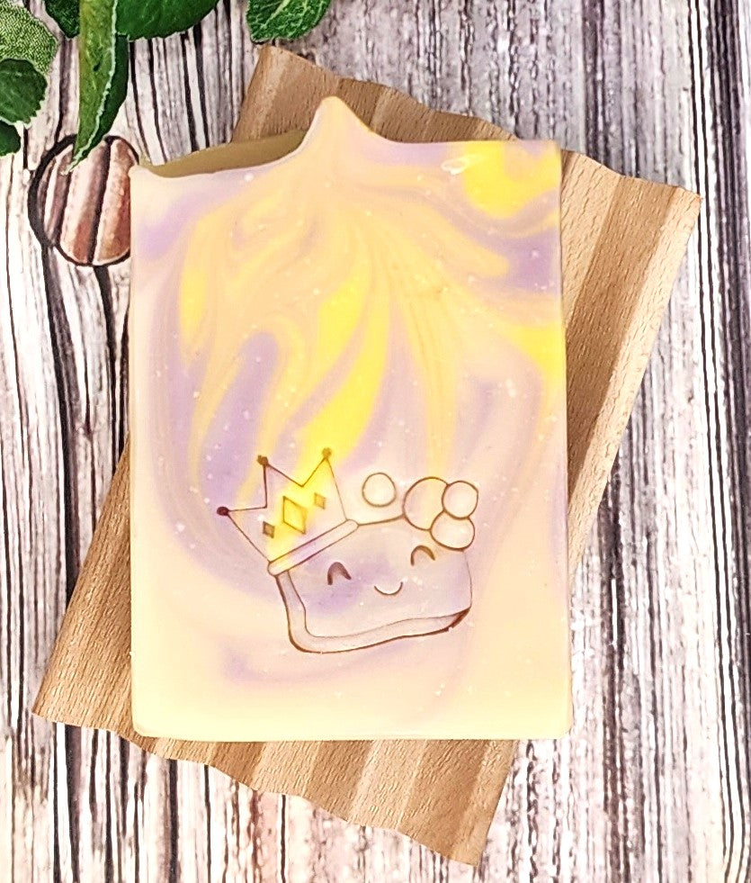Yellow & Purple soap with a character wearing a crown on a wooden soap dish.