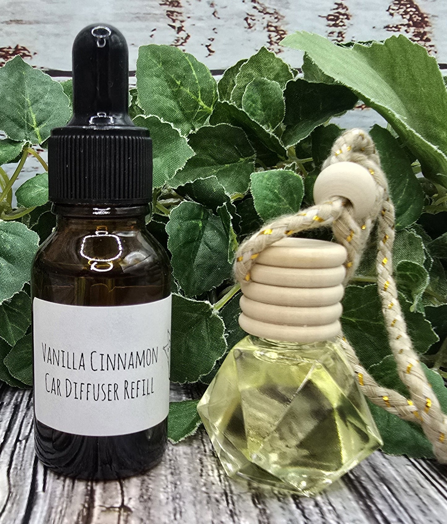 Vanilla Cinnamon car diffuser & refill bottle on a wooden surface with green leaves in the background.