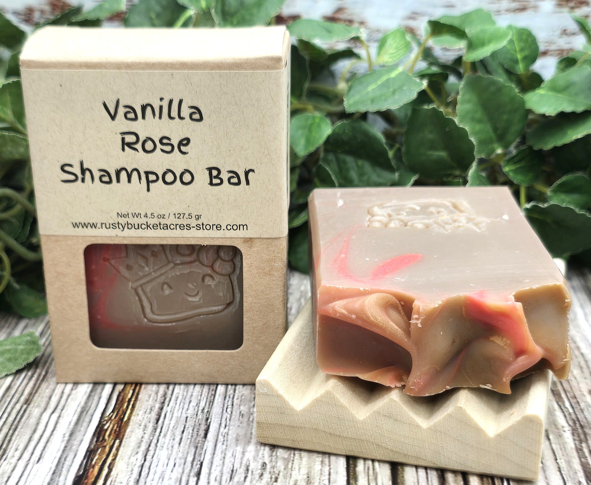 Vanilla Rose shampoo bar with packaging on a wooden surface with green leaves in the background