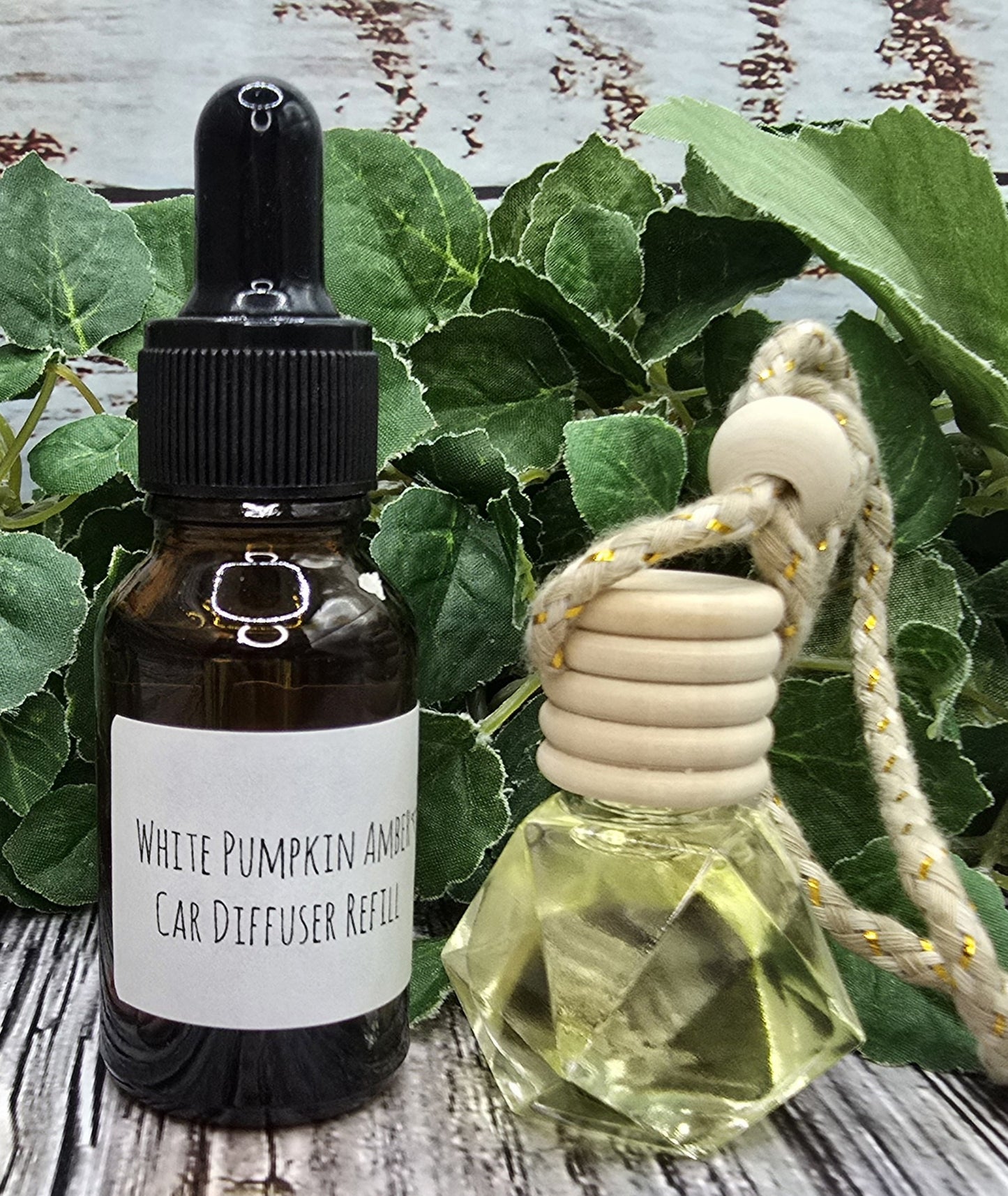 White Pumpkin Amber car diffuser & refill on a wooden surface with green leaves in the background.