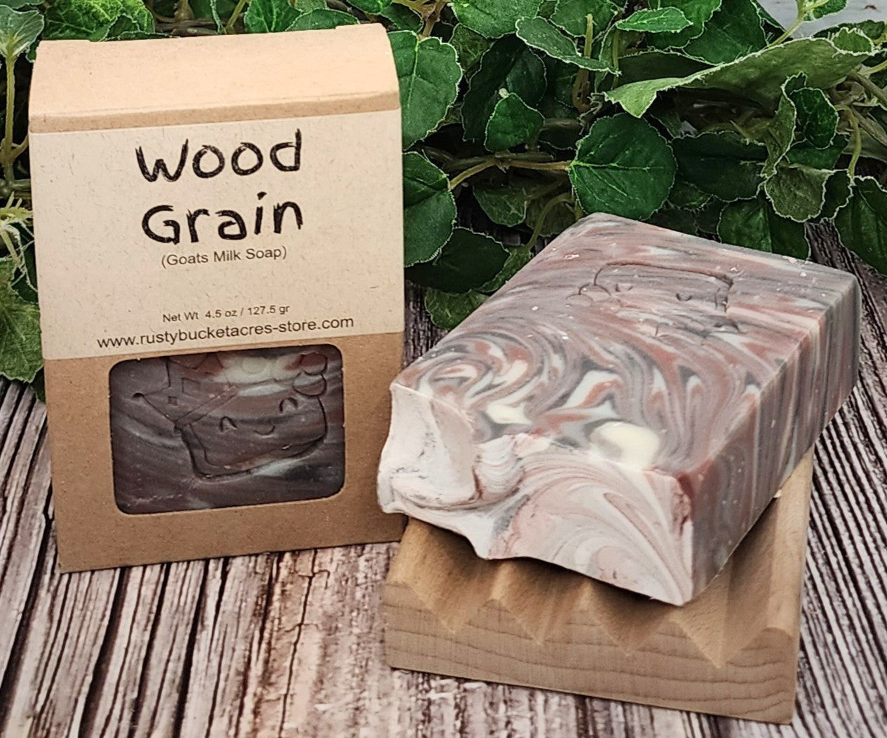 Goats milk soap with 'Wood Grain' packaging on a wooden surface with greenery in the background