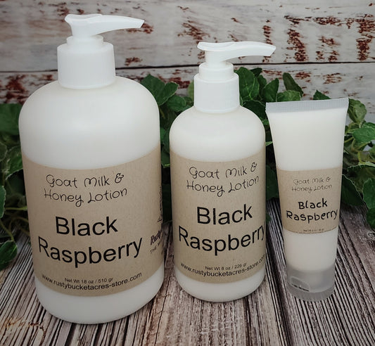 Three bottles of Black Raspberry Goat Milk & Honey Lotion on a wooden surface with greenery.
