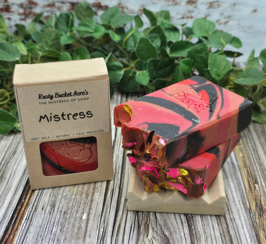 Bar of soap with a 'Mistress' packaging on a wooden surface with greenery in the background