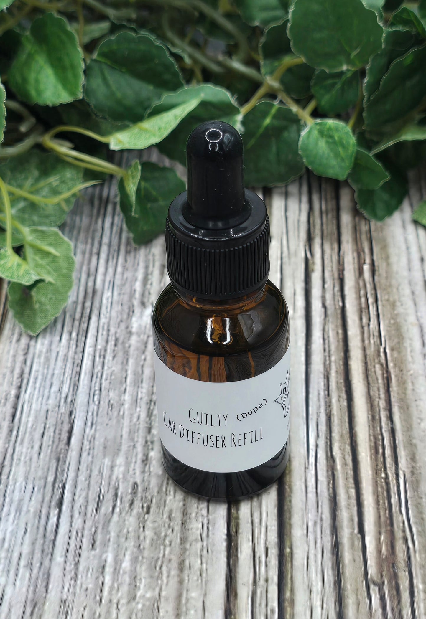 Bottle of Guilty Co. diffuser refill on a wooden surface with green leaves in the background