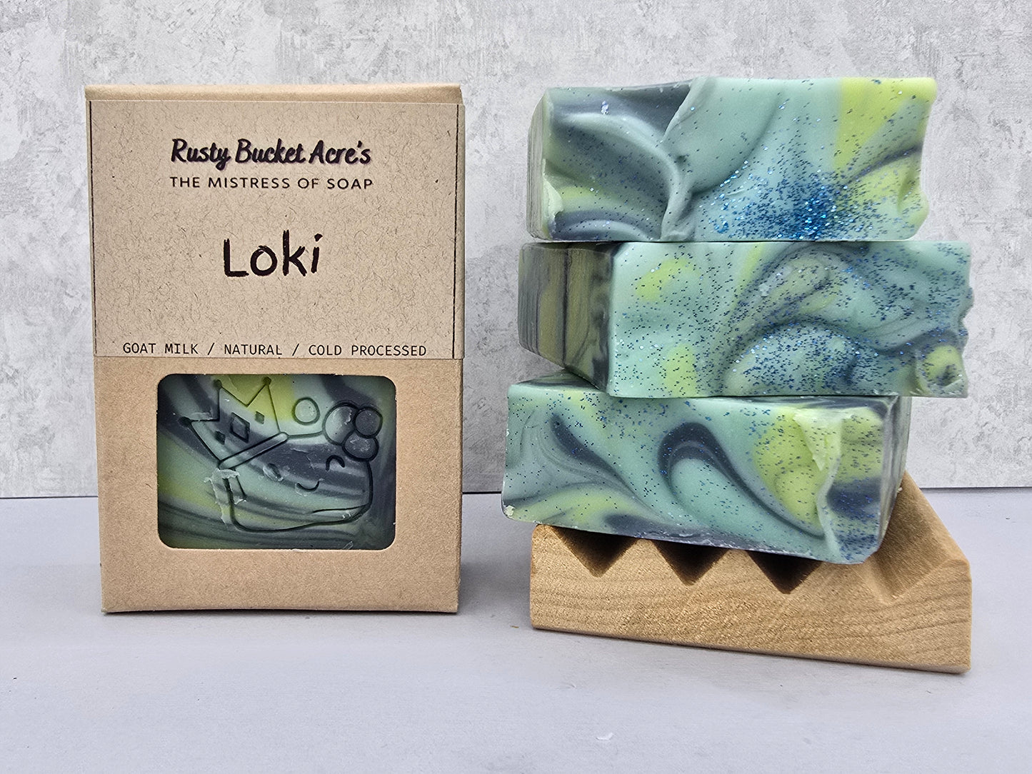 Loki handcrafted soap bars with visible green & blue colors, shown next to their kraft paper packaging box labeled 'Rusty Bucket Acre's Loki'.