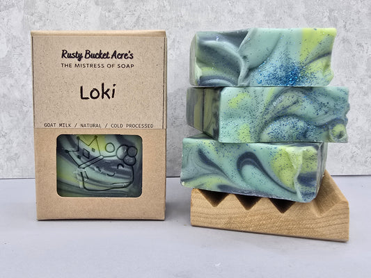 Loki handcrafted soap bars with visible green & blue colors, shown next to their kraft paper packaging box labeled 'Rusty Bucket Acre's Loki'.
