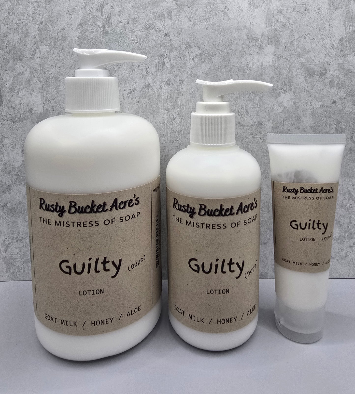 Two bottles and a tube of Rusty Bucket Acres Guilty Dupe lotion on a gray background